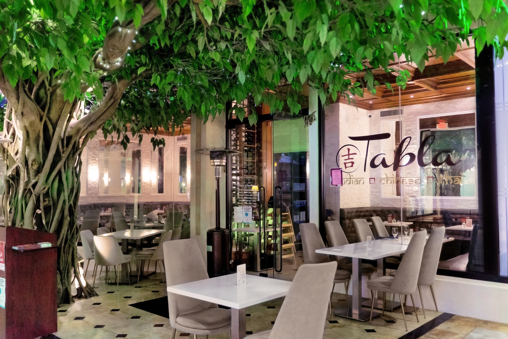 The front of Tabla restaurant shows a live tree hovering above the entrance door, along with tables outside.