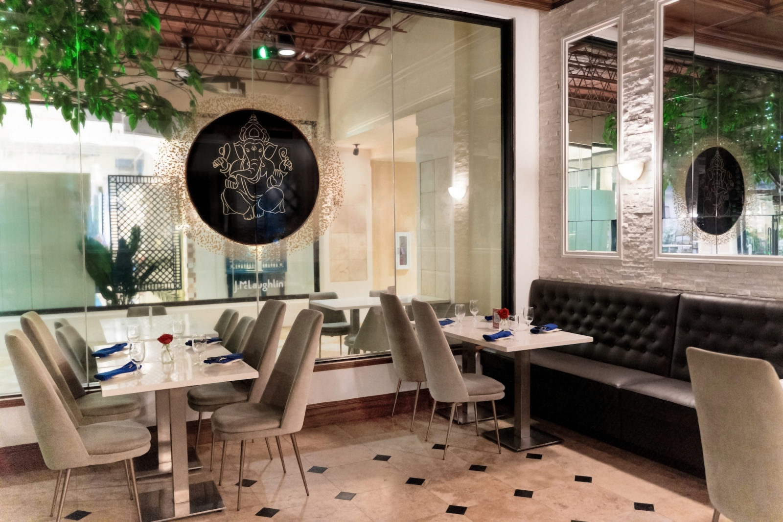 Inside dining area at Table with neutral chairs, white tables, tiled floors, and a leather booth against the wall.