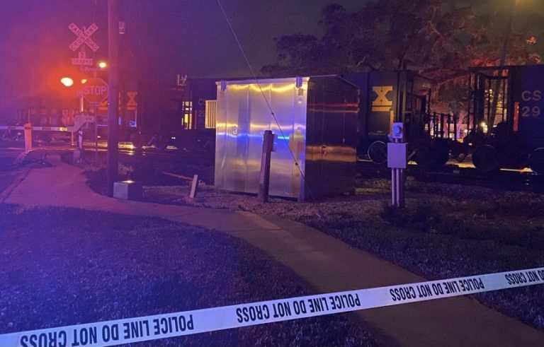 Crime scene tape blocks locals from entering the scene in front of the train tracks with red railroad crossing lights.