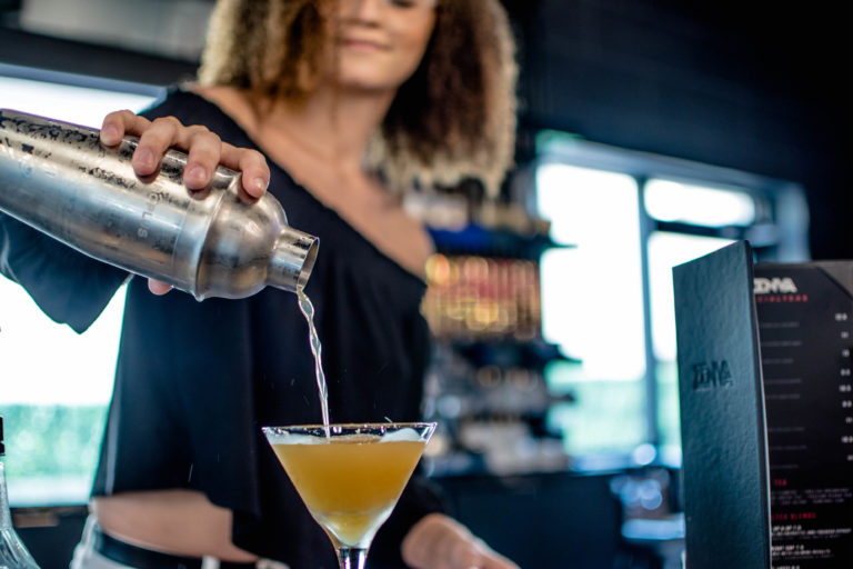 Woman pours a drink into a martini glass behind a bar.