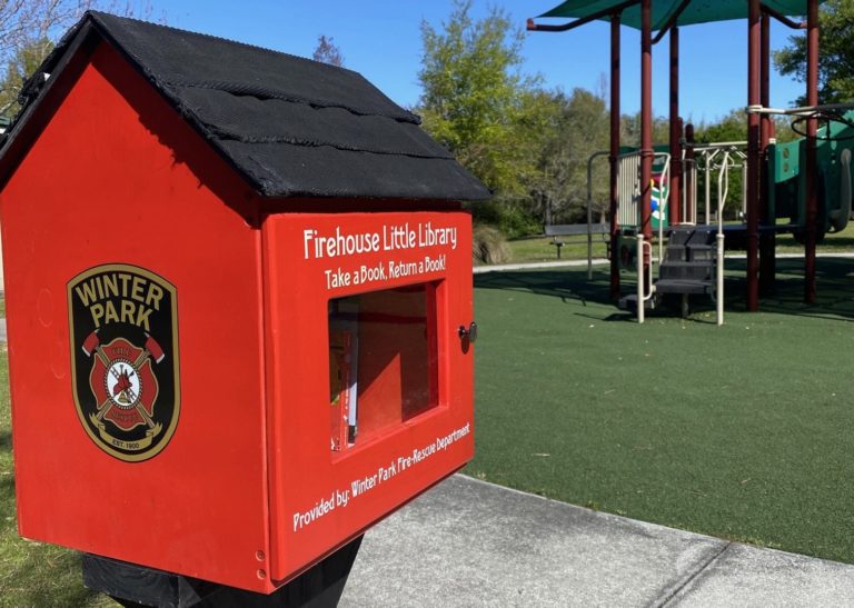 A red little library shows the Winter Park Fire-Rescue Department badge and there is a playground in the background.