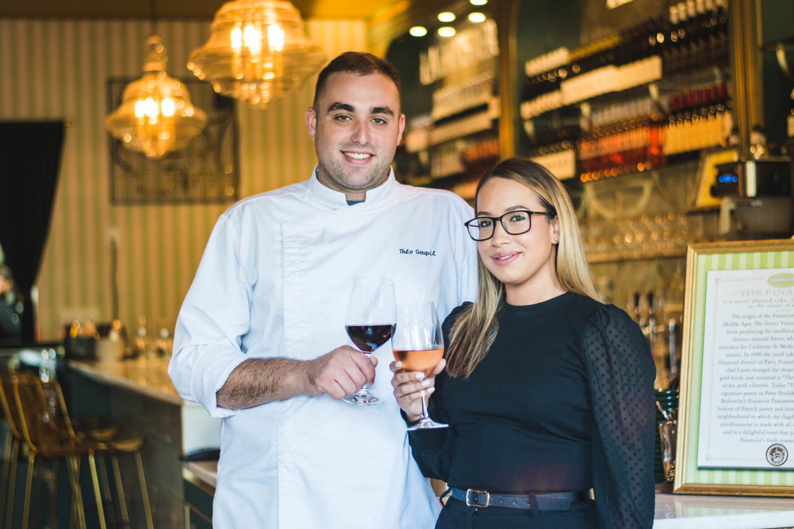 Chef Théo and Danielle Goupil cheers wine glasses in front of the Financier Bistro.