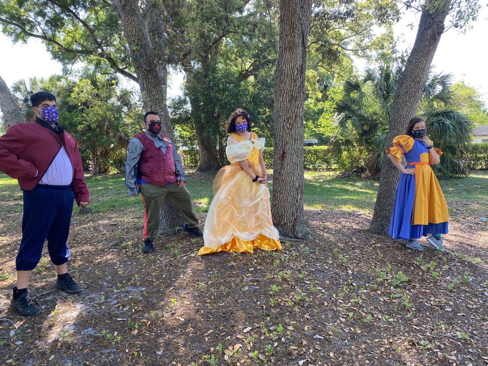 Image shows four actors dressed up as members of the Beauty and the Best cast standing outside in front of trees.