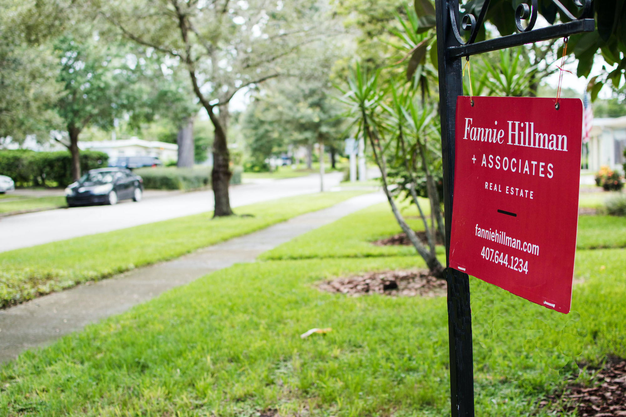 A red Fannie Hillman real estate sign posted in a front lawn.