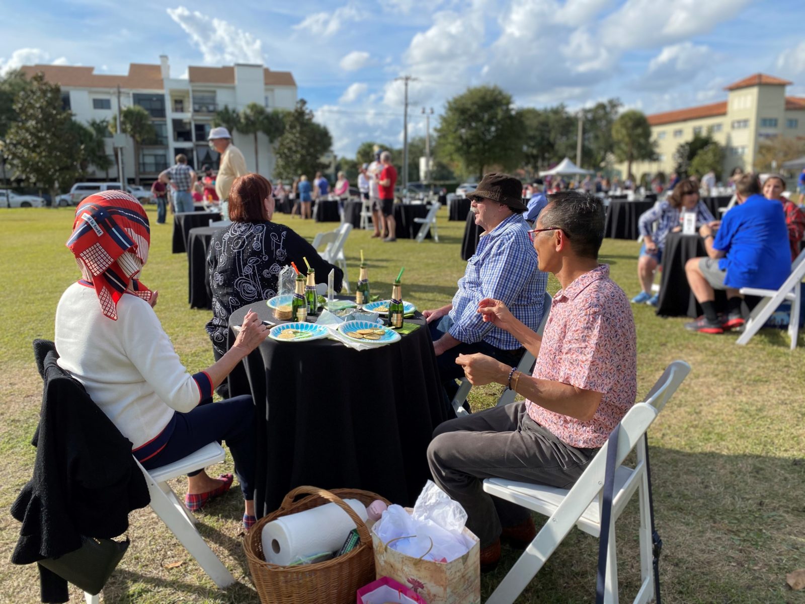 A white table with four people and a black tablecloth with food, drinks, and shopping bags. 