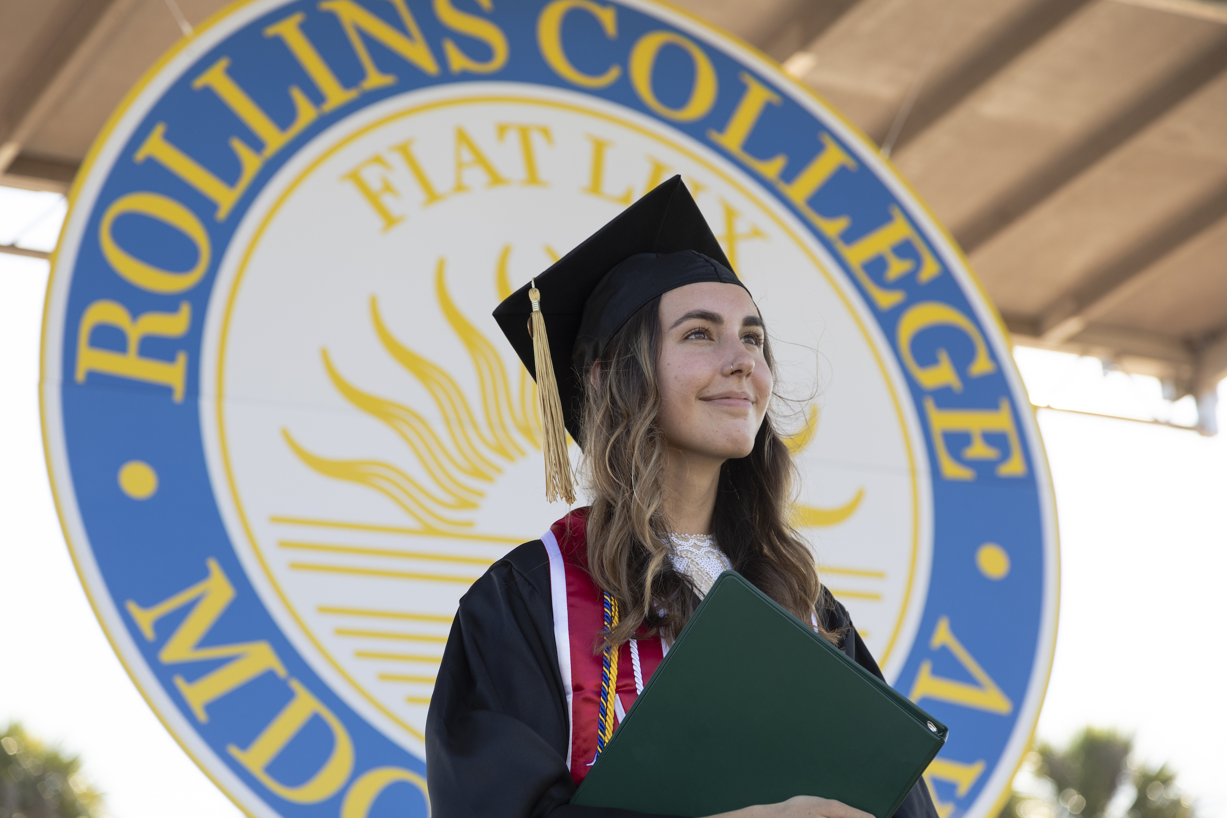Photo shows graduate holding diploma in front of the Rollins College crest.