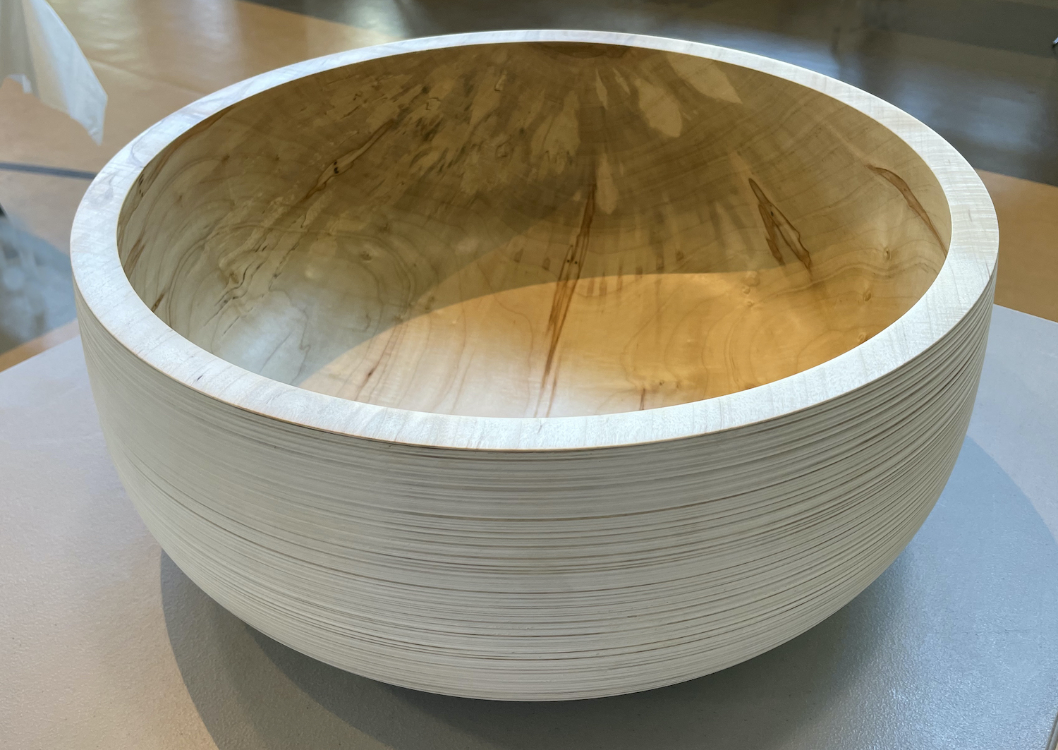 Wooden bowl made out of light and Carmel colored wood is sitting on a table. 