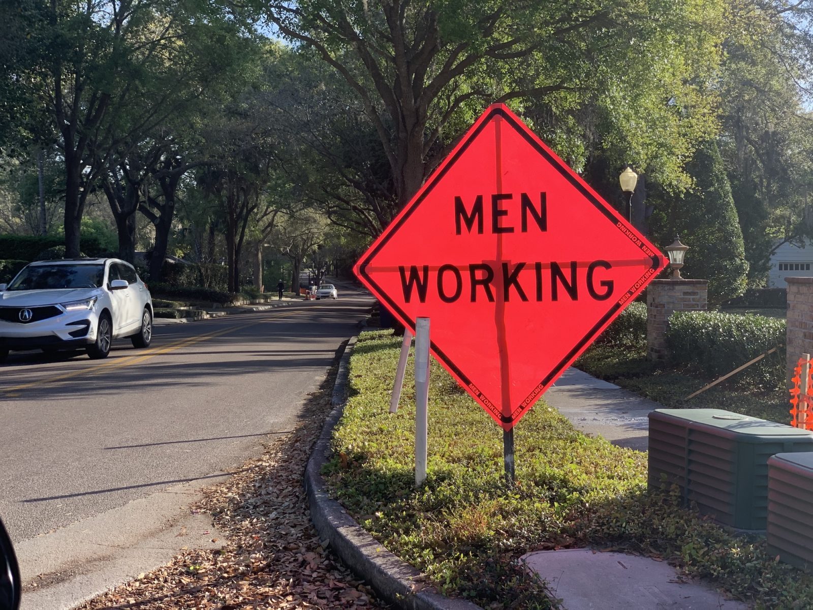 A large, orange "Men Working" sign propped up on a sidewalk.