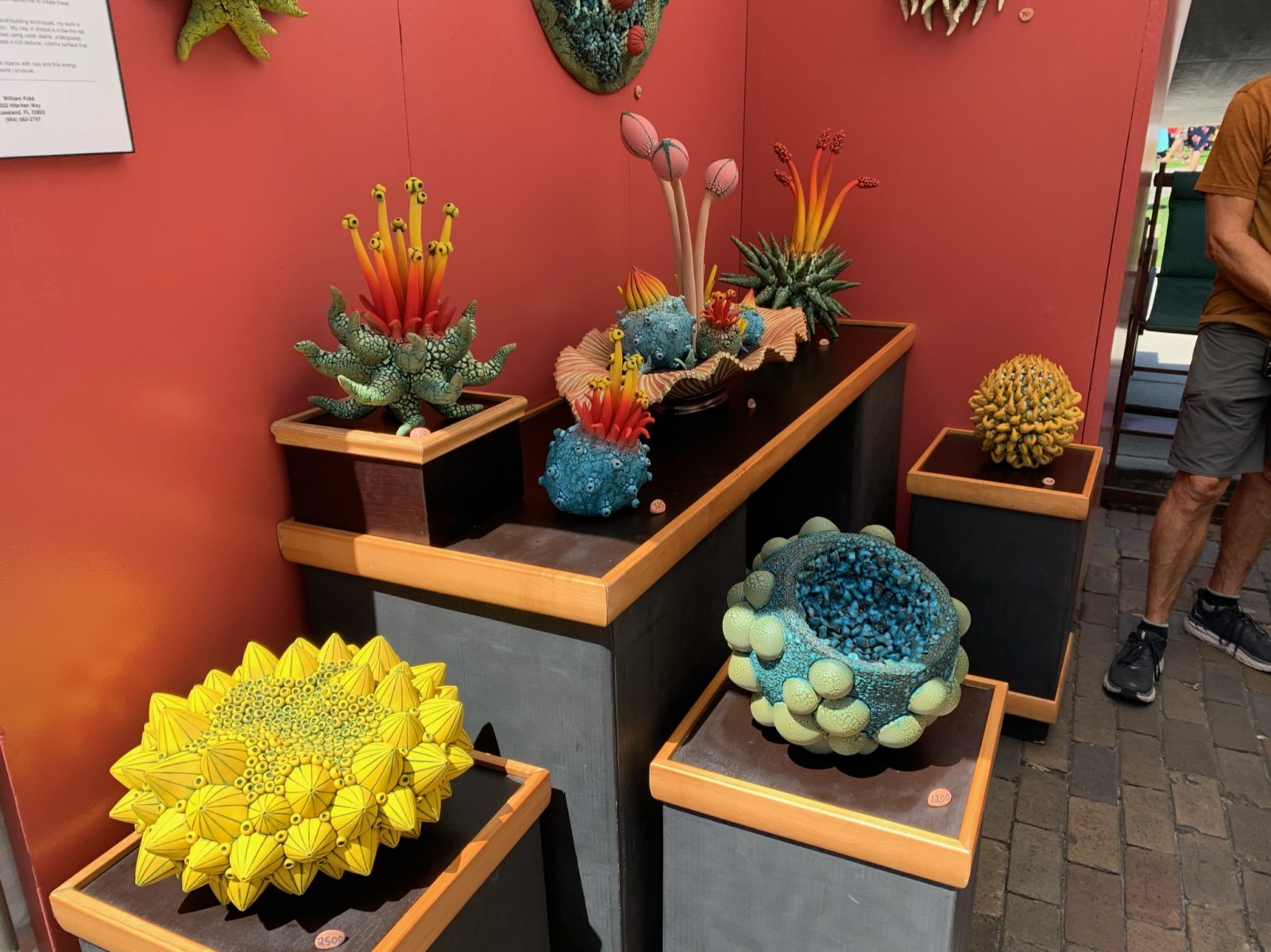 Red walls are the background for various clay sculptures made out of bright colors, mirroring cacti and other plants.