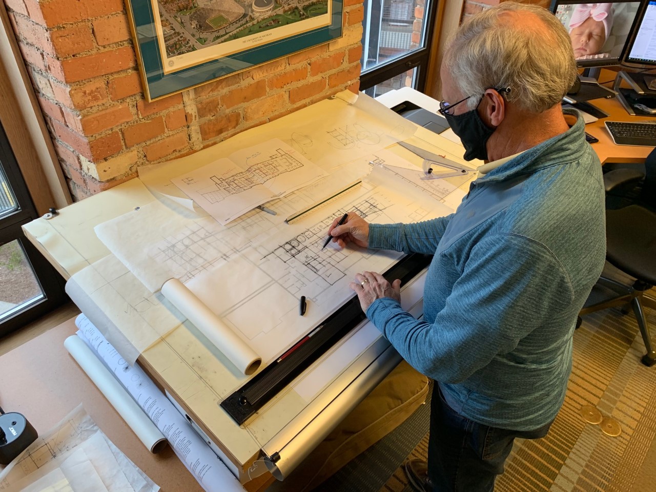 Image shows a man sketching plans on large architectural paper.