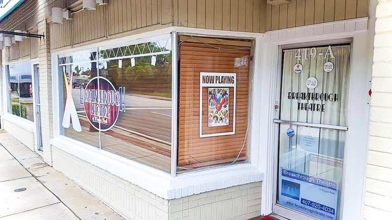 Building with large window and brown shades and a sign that says now playing.