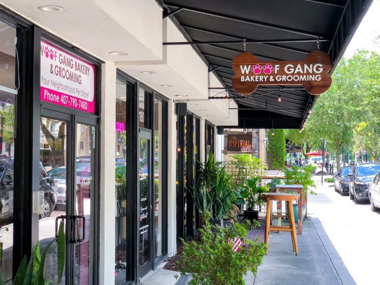 Building with black roof, white walls, green landscape, and a pink sign that says Woof Gang