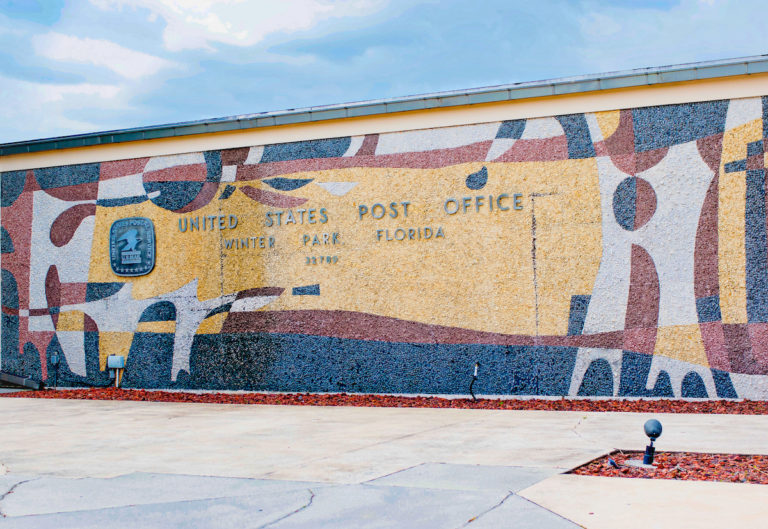 Wall with blue, red, and beige mural says United States Postal Service