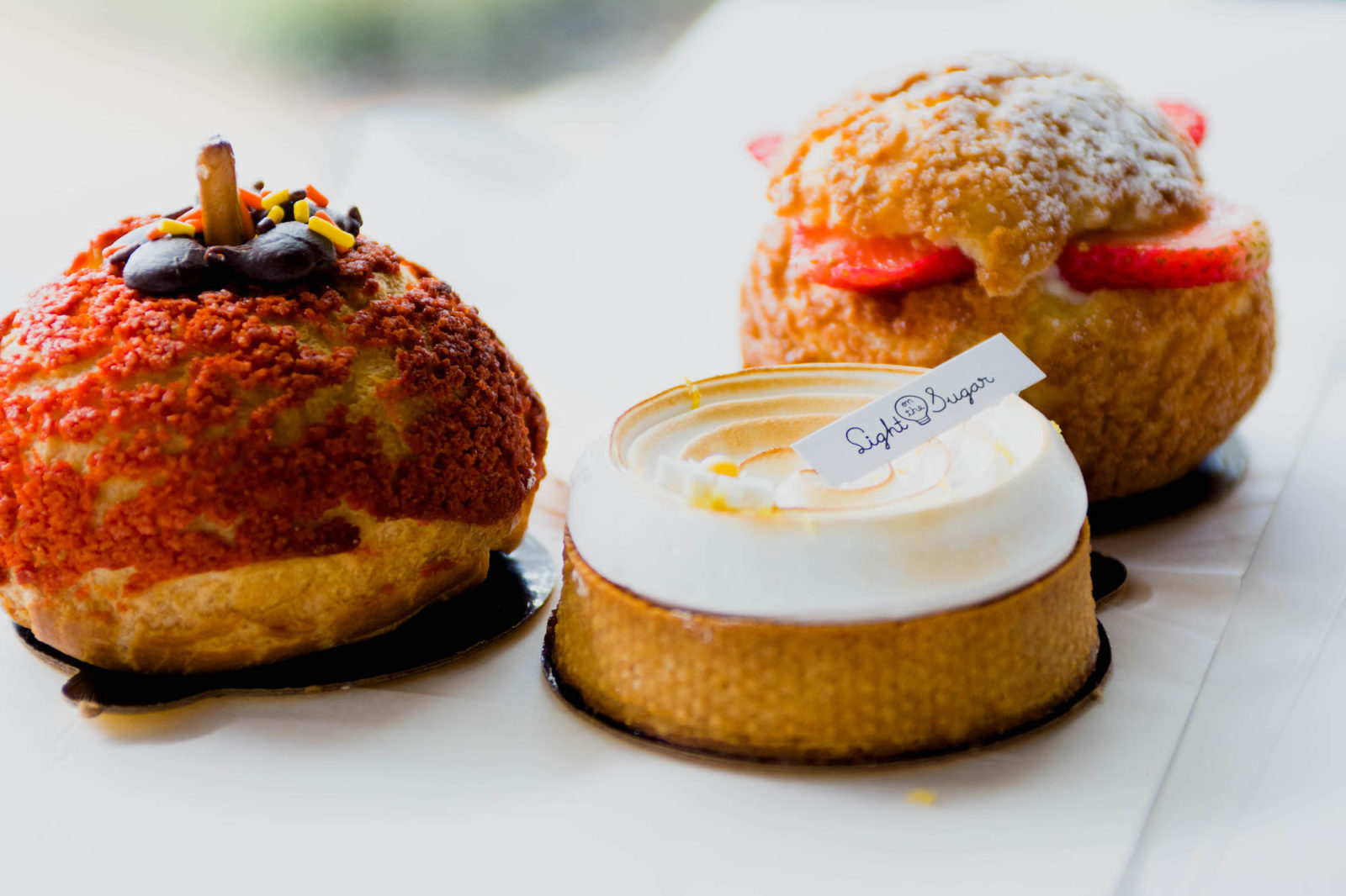 Three pastries sit on a white surface, one of which has a "Light On The Sugar" tag.